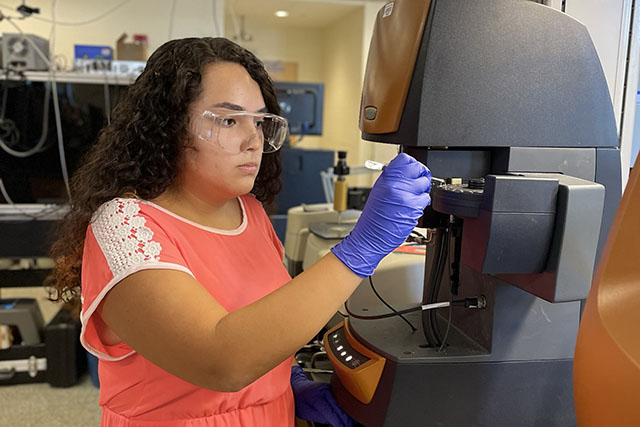 undergraduate student in white lab coat sets up a test on scientific equipment